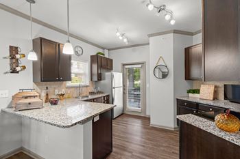 A kitchen with hardwood floors, granite countertops, stylish lighting, dark cabinets, and stainless steel appliances.